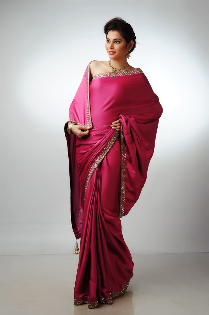 Stylish Indian woman in a vibrant pink saree posing gracefully in a studio setting.